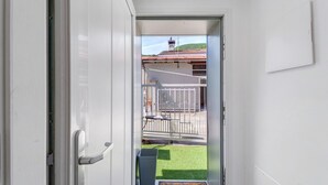 Ein Flur, der zu einem Balkon mit Metallgeländer, einem kleinen Tisch und einem Mülleimer führt.