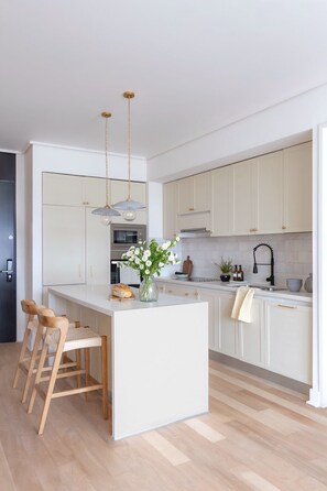A modern kitchen with a central island, wooden stools, a hanging light fixture, and a potted plant. - Vespucio Harmony 2D con Wifi (Santiago)
