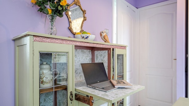 Ein Zimmer mit einem grünen Schrank, der Küchenutensilien enthält, einem Laptop darauf und einem Spiegel.