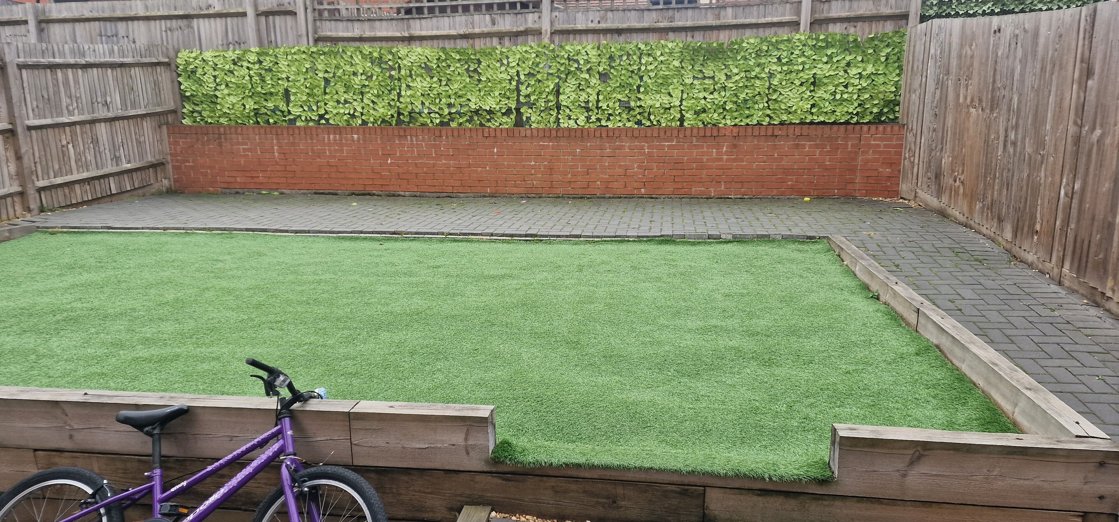 Ein Garten mit Kunstgrasanlage, Holzzaun und Mauerwerk.