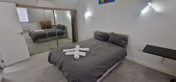 A bedroom with a bed, a mirror, a bedside table, and a wall-mounted shelf.