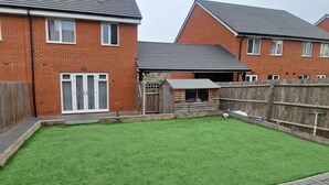 A residential backyard with a well-maintained lawn, a wooden fence, and a small wooden structure.