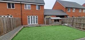 Un jardin arrière d’une maison, avec une pelouse bien entretenue, une clôture en bois et une petite construction en bois.