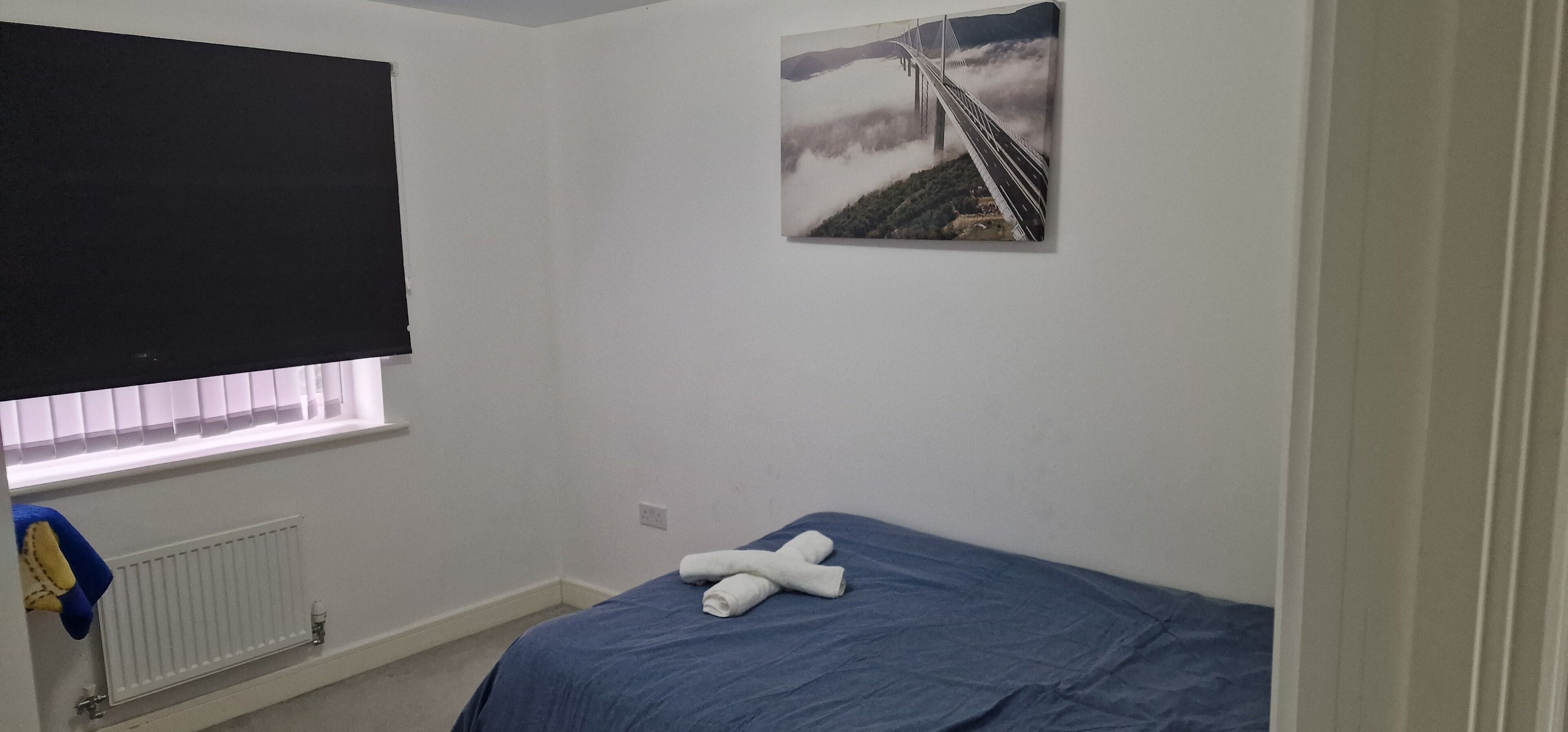 A bedroom with a bed, a window with blinds, a radiator, and a picture on the wall.