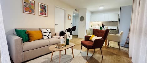 Een woonkamer met een bank, fauteuil, salontafel en een keuken op de achtergrond.