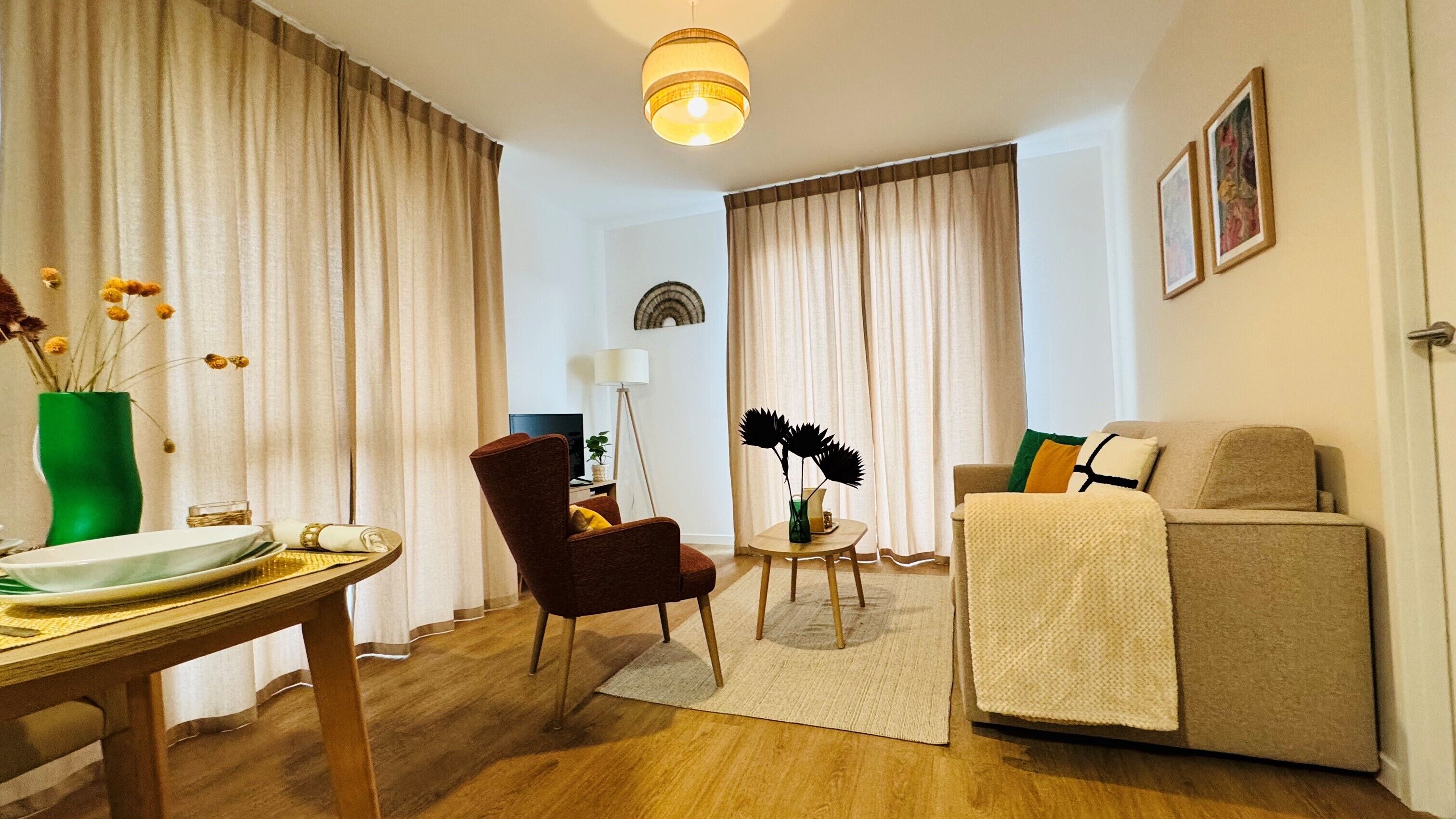 A living room with a sofa, a chair, a table with a vase, and curtains.