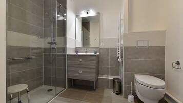 A modern bathroom with a glass shower enclosure, a toilet, a sink with a mirror, and a small trash bin.