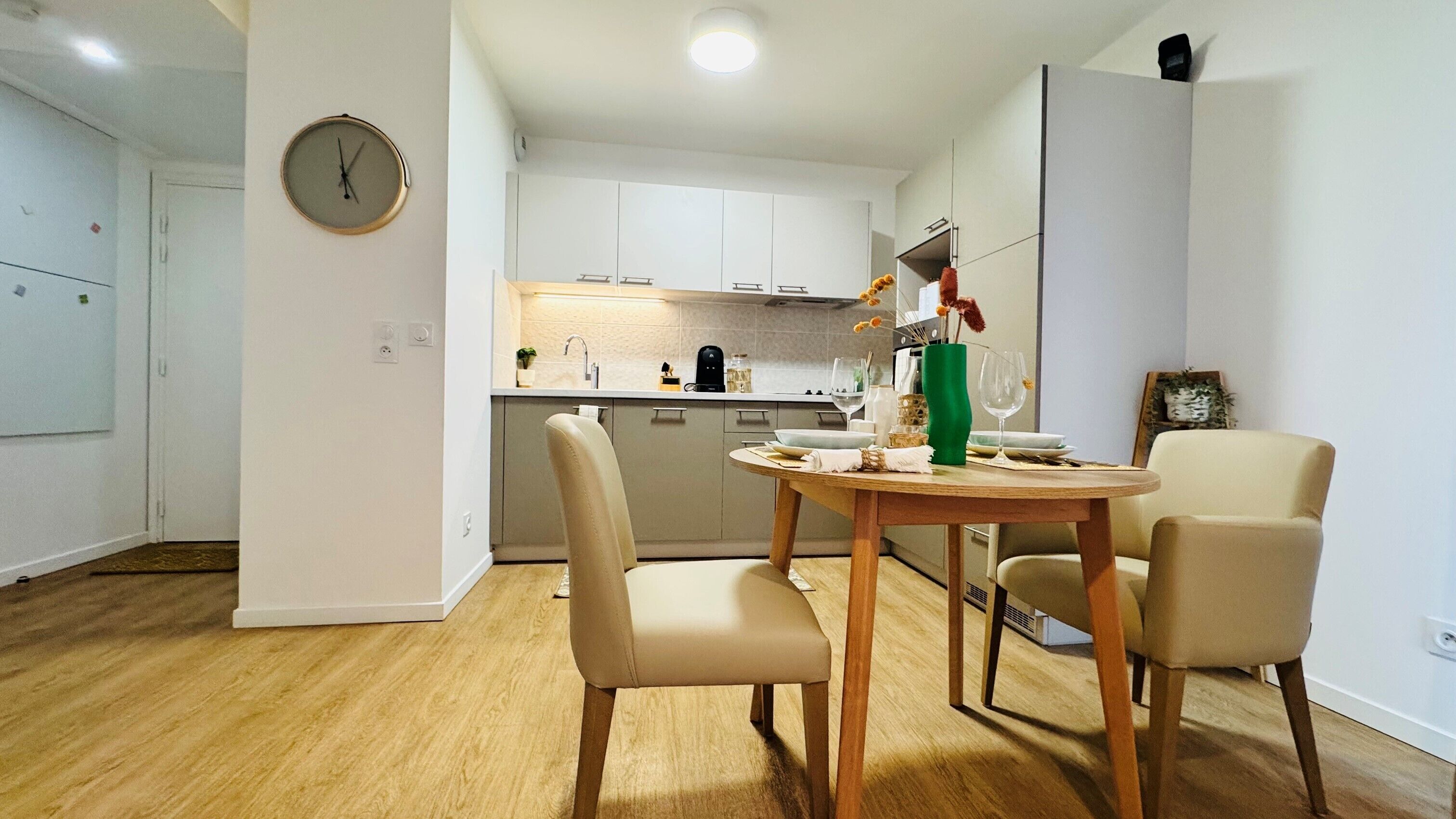 A modern kitchen with white cabinets, a dining table with chairs, and a clock on the wall.