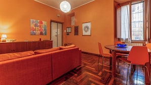 A cozy living room with a sofa, a dining table with chairs, a wooden floor, and a window with curtains. - Casa Anna - Vatican City  (Rome)