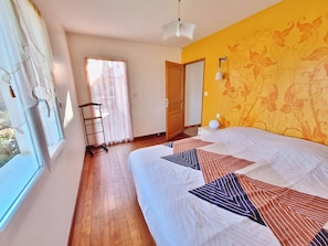 A bedroom with a bed, a window, a door, and a wall with a floral pattern.