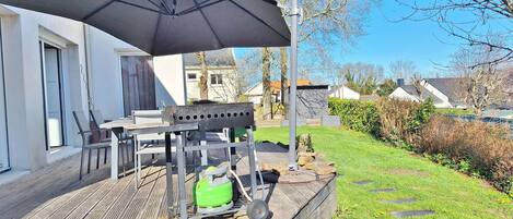 Un patio al aire libre con una mesa, sillas, una parrilla y un gran paraguas.