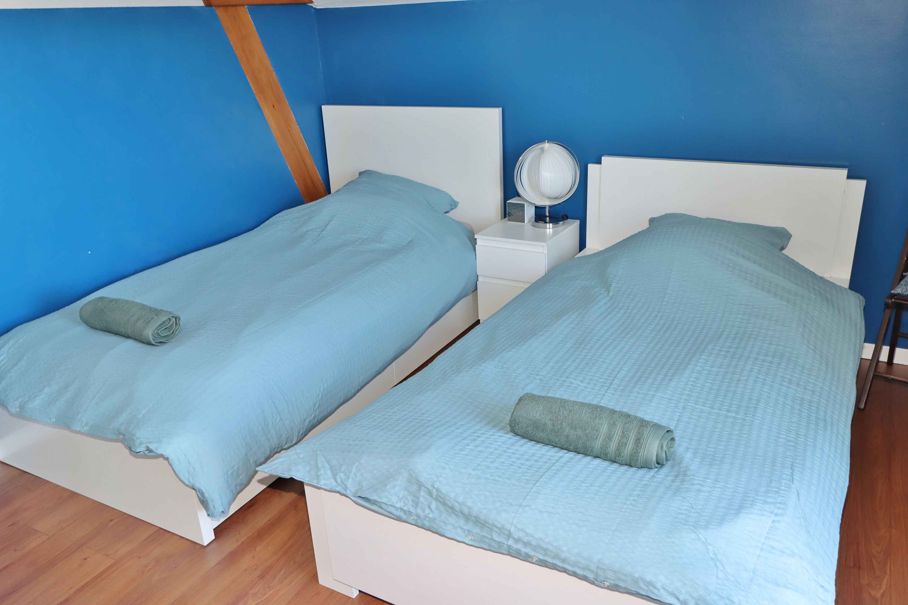 Deux lits jumeaux avec une parure de lit bleue assortie et une petite table de chevet avec un miroir.