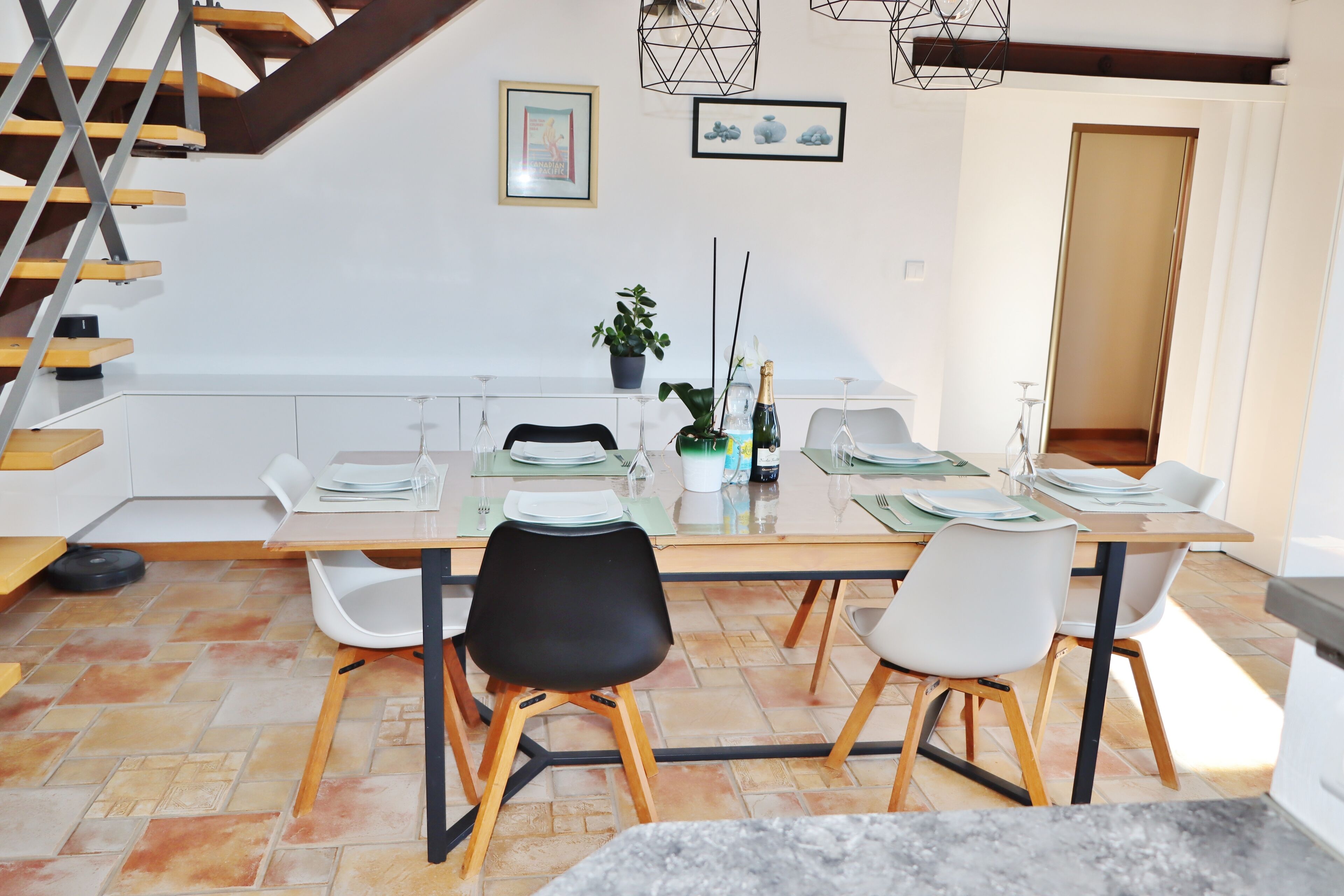 A dining area with a wooden table, white chairs, a potted plant, and a staircase.