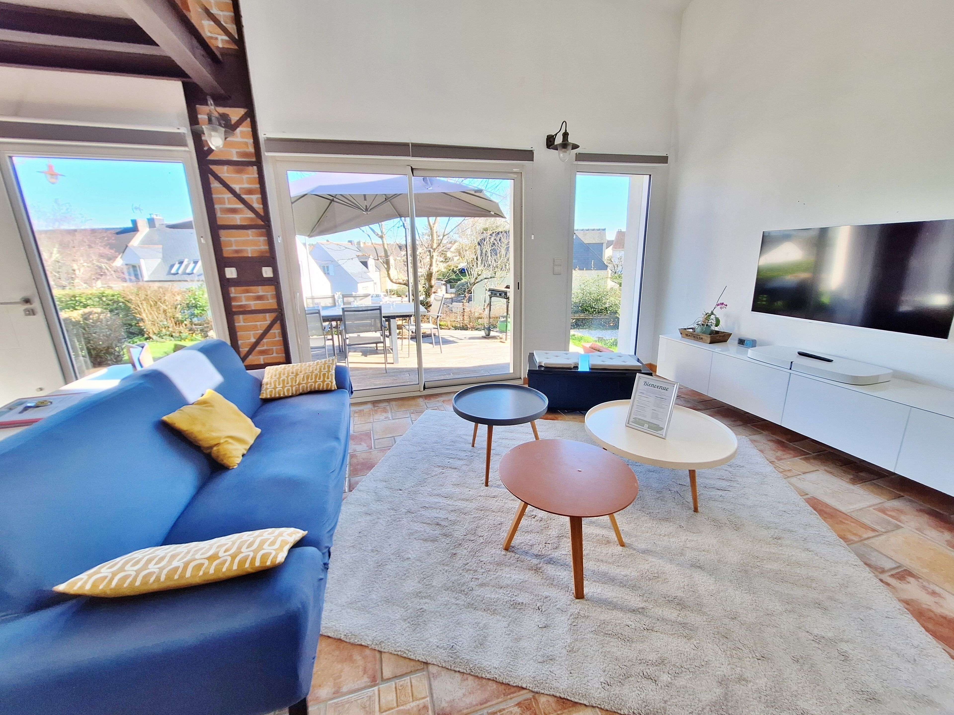 A modern living room with a blue sofa, a TV, a coffee table, and a sliding glass door leading to an outdoor patio.