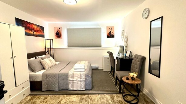 A bedroom with a bed, a desk, a chair, a mirror, and artwork on the walls. - Room-saint John - Wi-fi - 4mins Regional (Saint John)