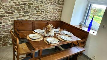 Un comedor con pared de piedra, bancos de madera, una mesa dispuesta con platos, vasos y un adorno decorativo.