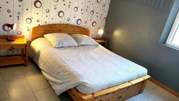 A neatly made bed with a wooden headboard, a bedside table with a lamp, and a patterned wall.