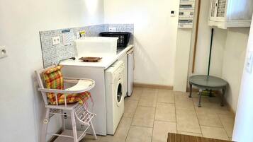 Un área de lavandería con lavadora, secadora y una pequeña mesa con una silla.