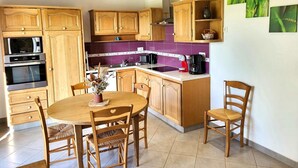Eine Küche mit Holzausstattung, einem Esstisch mit Stühlen, einer Mikrowelle, einem Backofen und einer Kaffeemaschine.