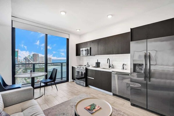A modern kitchen with a large window, a dining area with a table and chairs, and a view of the cityscape. - Lux Studio at Downtime  Miami & Bay Views (Miami)