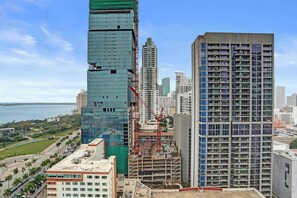 Um edifício alto com fachada de vidro moderna, rodeado por outros edifícios altos e uma grua de construção.
