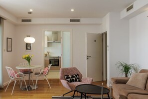 Ein modernes Wohnzimmer mit Essbereich, einer Küche im Hintergrund und einer Tür zu einem weiteren Zimmer.