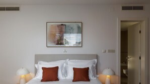 Una camera d'albergo con un letto, due comodini, un tavolino di fianco al letto, un quadro appeso al muro e una porta che dà su un bagno.