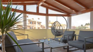 Um terraço com área de estar ao ar livre, uma cadeira suspensa e uma mesa com copos.
