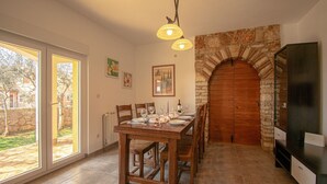 Uma área de refeições com lareira de pedra, uma mesa de madeira posta para quatro pessoas e uma janela grande.
