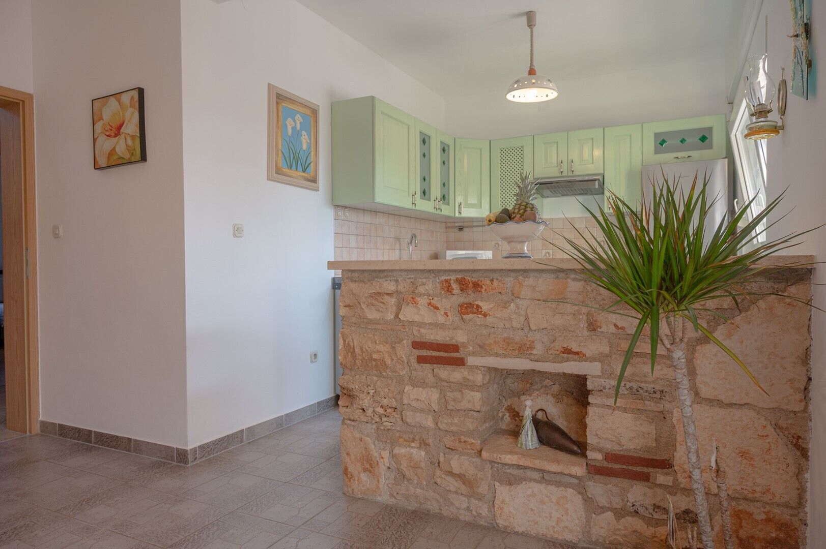 A kitchen with light green cabinets, a stone island, and a hanging light fixture.