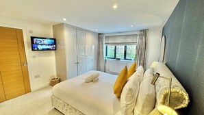 A bedroom with a bed, a television mounted on the wall, a window with curtains, and a door. - Modern Luxury Home - Hot Tub - 3 King Bedrooms - Free Parking - Close to Beaches (Poole)