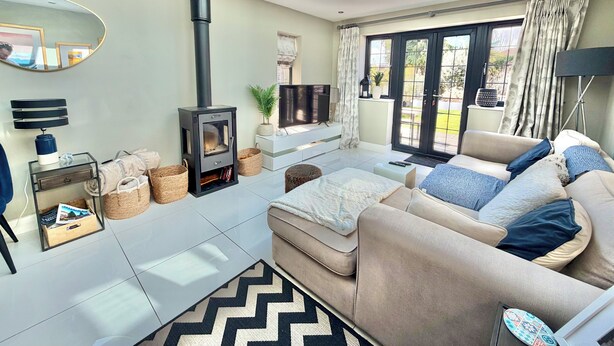 A modern living room with a sofa, a TV, a fireplace, and a skylight. - Modern Luxury Home - Hot Tub - 3 King Bedrooms - Free Parking - Close to Beaches (Poole)