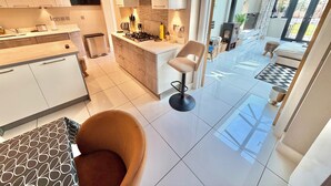 A modern kitchen with a central island, a dining area with a chair, and a view of the outdoor patio. - Modern Luxury Home - Hot Tub - 3 King Bedrooms - Free Parking - Close to Beaches (Poole)