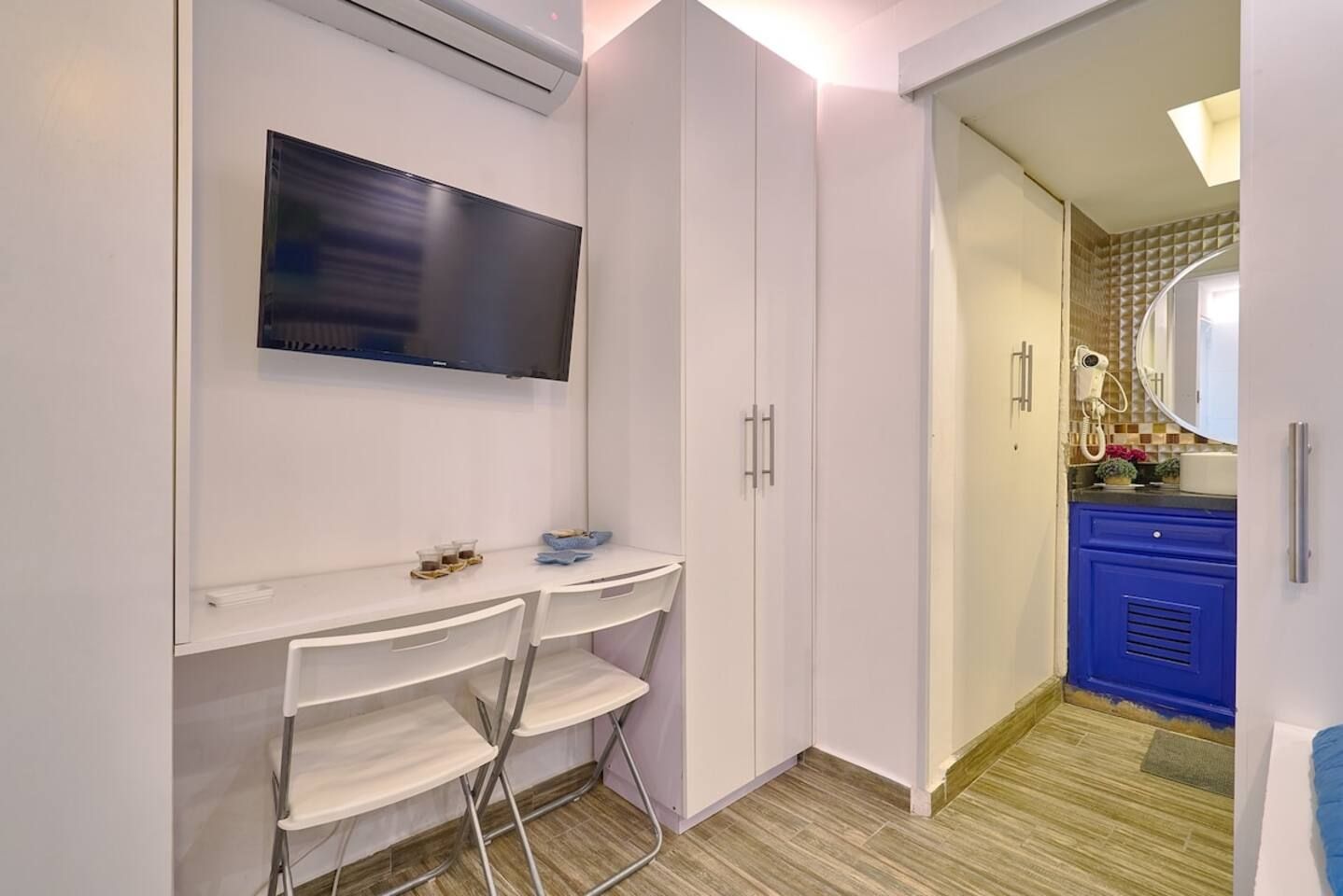Una habitación compacta con una televisión de pantalla plana montada en la pared, un escritorio pequeño con una silla y un mueble azul.