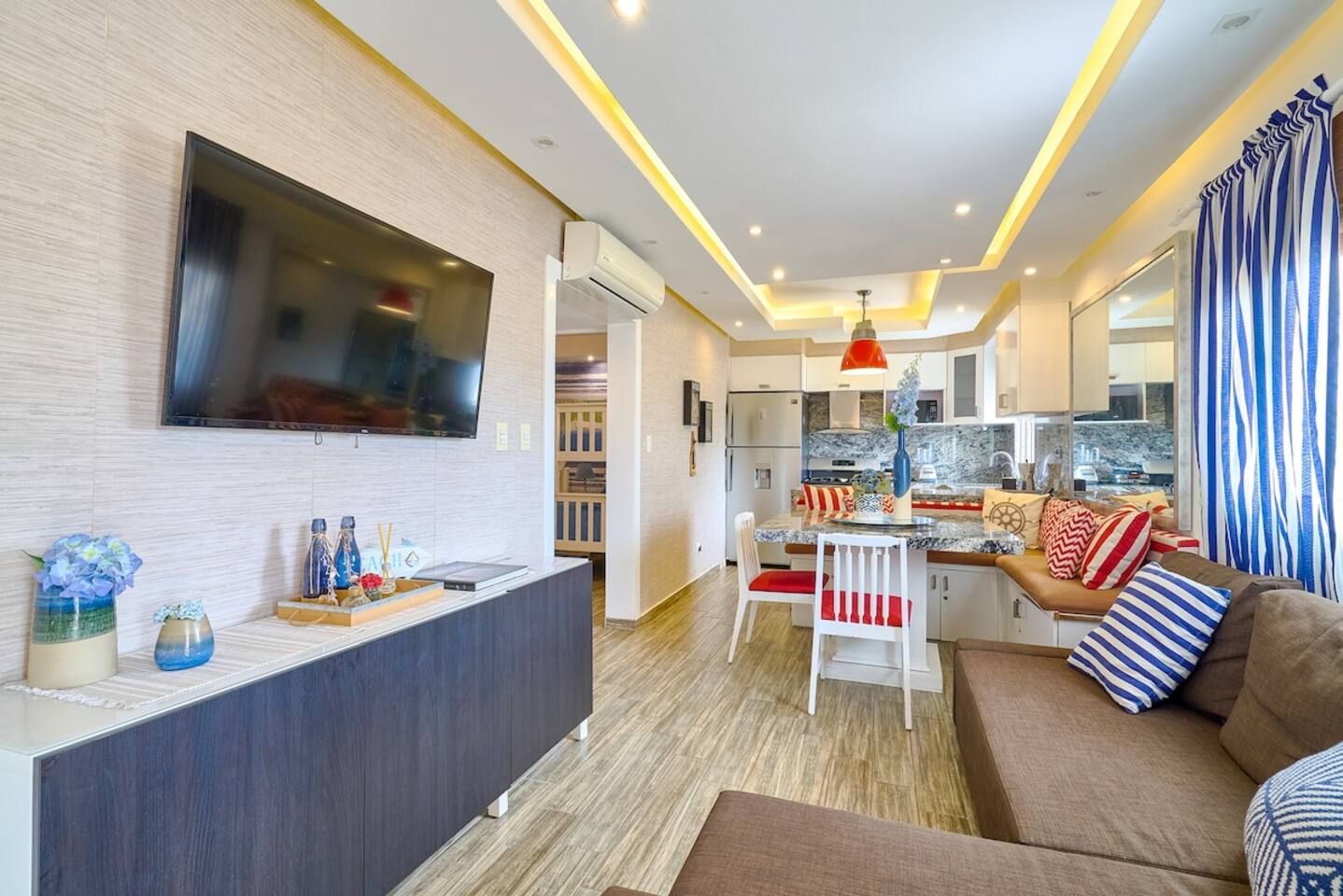 Una sala de estar moderna con un televisor de pantalla plana, una zona de comedor y una cocina con encimera de mármol.