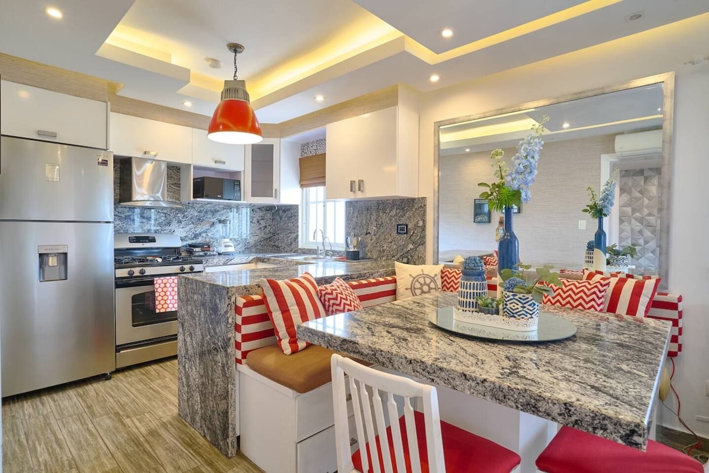 Una cocina moderna con una isla central, electrodomésticos de acero inoxidable y una lámpara colgante roja.