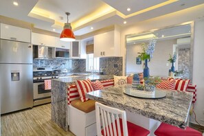 Une cuisine moderne dotée d’un îlot central, d’appareils électroménagers en acier inoxydable et d’un luminaire suspendu rouge.