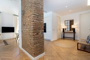 A modern living room with a brick accent wall, a flat-screen TV, a dining area with a white table and chairs, and a round rug. - Elegant 3BD apartment in Malaga. Plaza Marina II (Malaga)