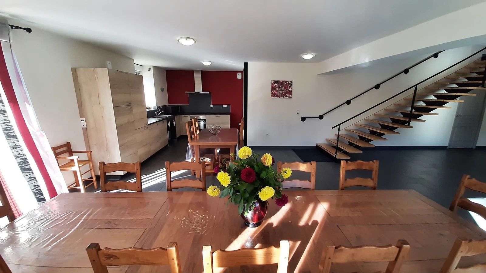A dining area with a wooden table and chairs, a vase of flowers, and a staircase in the background.