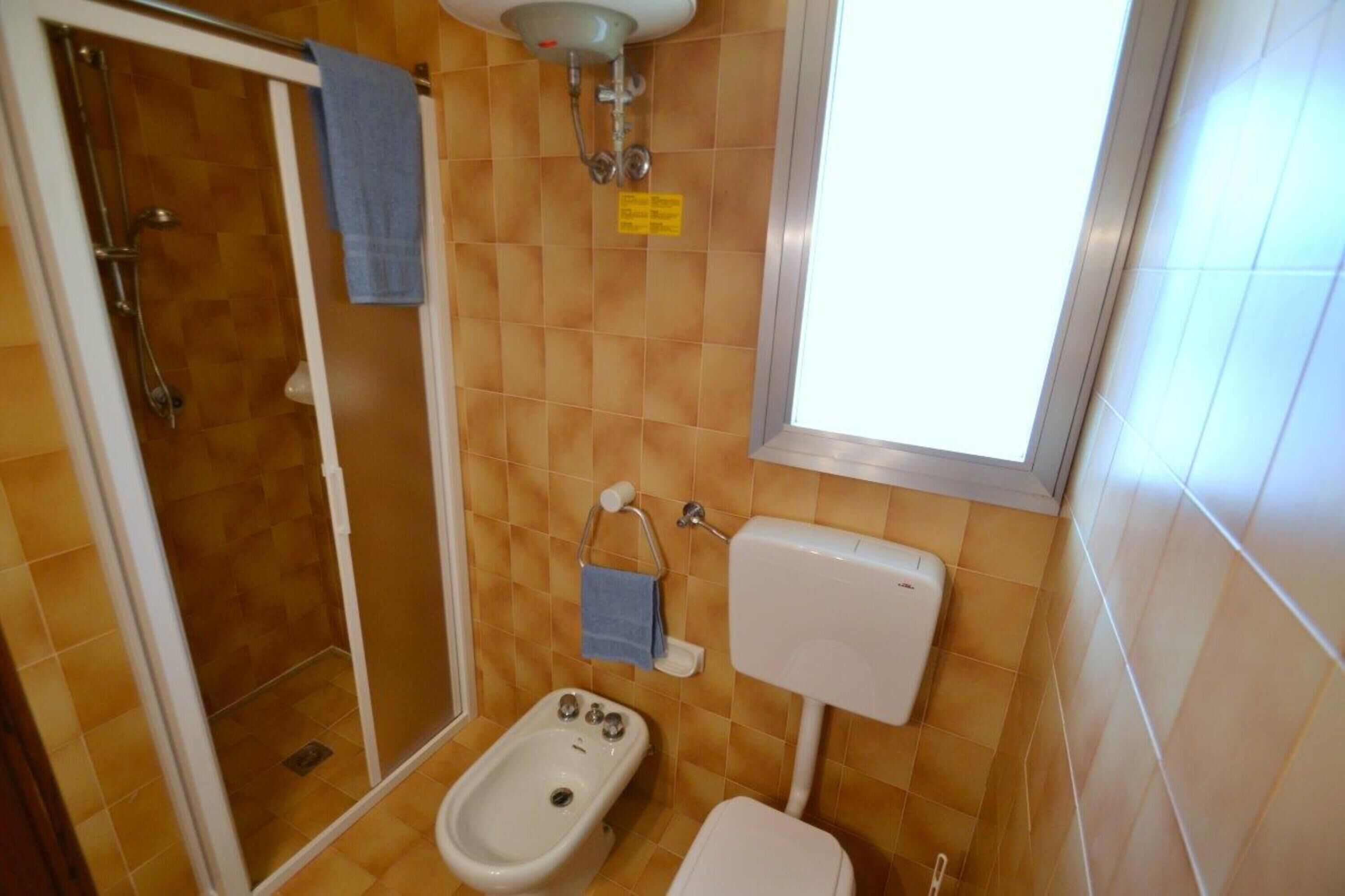 A bathroom with a shower, toilet, bidet, and a window.