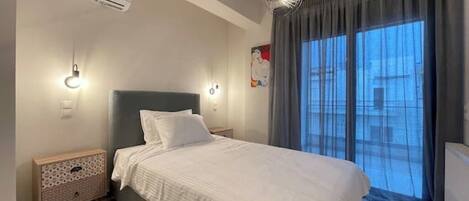 A bedroom with a bed, bedside tables, an air conditioner, a wall-mounted light, and a window with curtains.