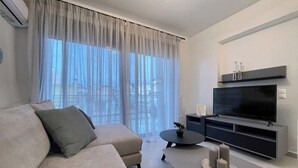 Un soggiorno moderno con un divano, un tavolino da caffè, una televisione a schermo piatto e un'ampia finestra con tende leggere.