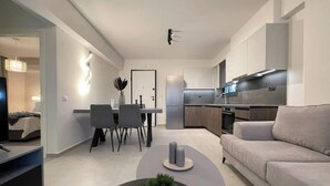 Un soggiorno moderno con un divano, un tavolino da caffè con una pianta, un'area pranzo con sedie e un tavolo, e una cucina con mobili e elettrodomestici.