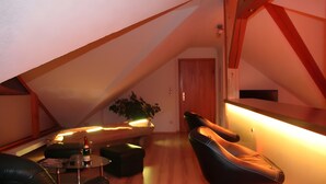 An attic room with a sloped ceiling, a black leather chair, a small table with a bottle, and a potted plant. - Holiday Apartment for 2 People (60 m²) in Sehmatal (Sehmatal)