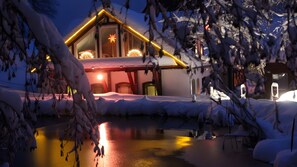 A snow-covered building with a lit interior, a snow-covered ground, and a reflective water surface. - Holiday Apartment for 2 People (60 m²) in Sehmatal (Sehmatal)