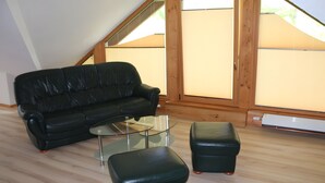 A room with a black leather sofa, a glass coffee table, and a matching ottoman. - Holiday Apartment for 2 People (60 m²) in Sehmatal (Sehmatal)