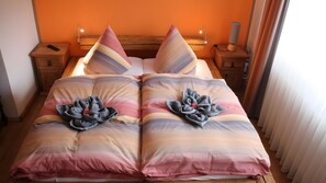 Un lit double avec une couverture à dégradé de couleurs, deux oreillers, une table de chevet avec une lampe et une petite table de nuit avec une lampe.