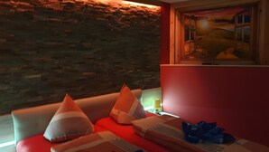 A room with a stone wall, a window with a sunset view, a sofa with pillows, and a lamp.