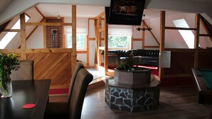 A room with a sloped ceiling, wooden beams, a fireplace, a pool table, and a billiards table.