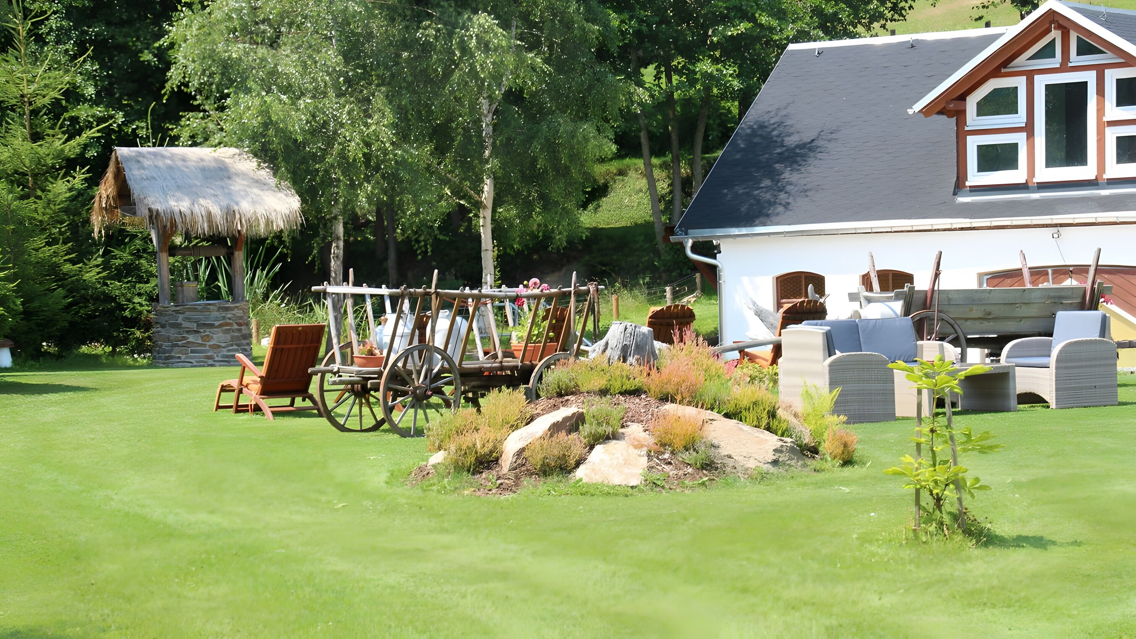 Una casa con un tetto di paglia, un carro di legno e mobili da giardino.